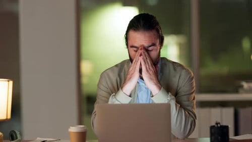 Frustrated business man suffering from a headache while working late in modern office