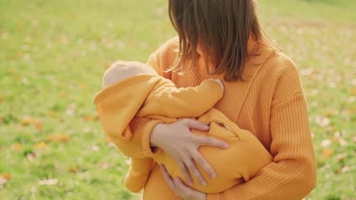 Mother Holds Baby Girl in Arms on Warm Autumn Day in Nature