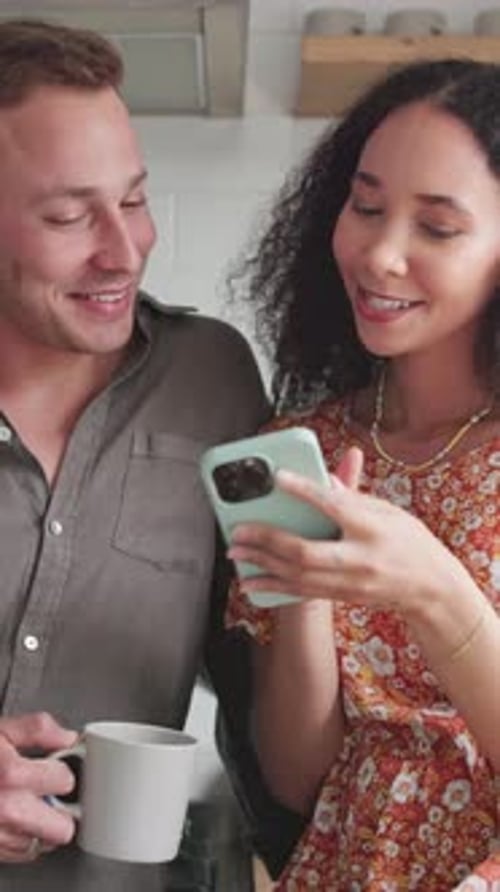 Smiling Couple Looking at Smartphone Together in a Bright Kitchen