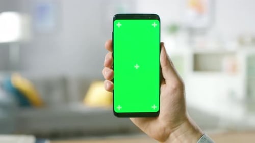 Close-up of a Man's Hand Holding Green Mock-up Screen Smartphone. Modern Mobile Phone. In the Backg