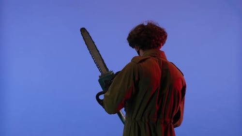 Man in White Mask with Chainsaw in Hands on Blue Background with Red Neon Light Image of Jason