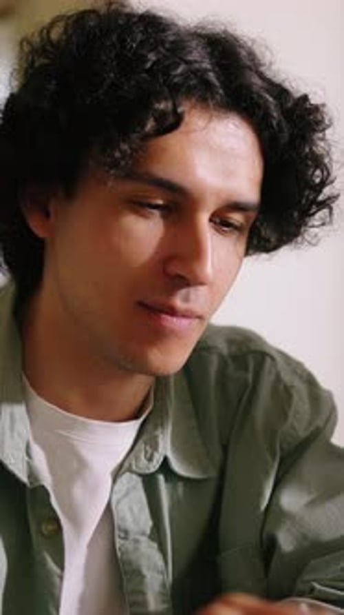 Young Man with Curly Hair Focused on Digital Work at Home Concentrating on Laptop Screen While