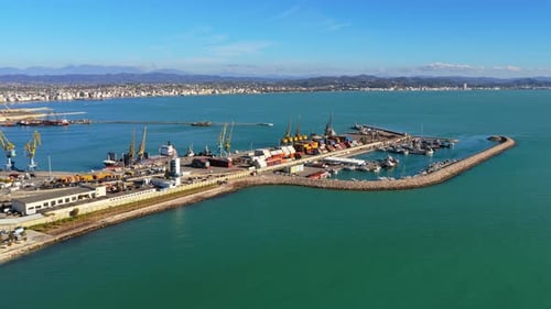 Aerial drone view of a busy container port, showing cargo ships, stacked colorful containers, indust