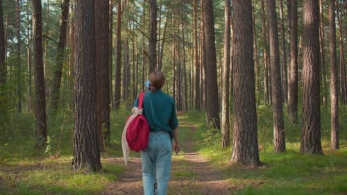 Friends Walking Through Lush Forest Path with Red Backpack and Draped Handkerchief