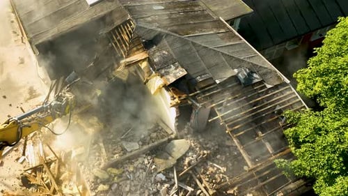 Aerial view showing an excavator claw tearing down a building's roof during a demolition project, wi