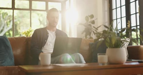 Man Using Laptop on Sofa in Brightly Lit Room