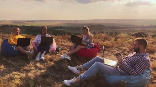 Colegas sentados em cadeiras próximas umas das outras com cadernos em uma clareira ao pôr do sol em um dia de verão