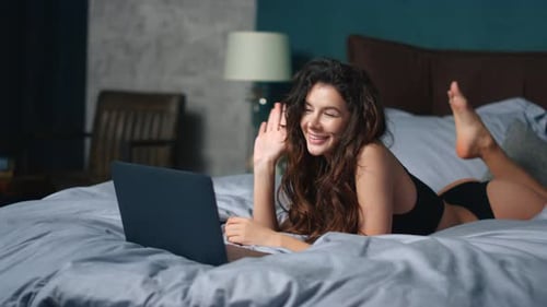 Jovem alegre em lingerie cumprimenta o interlocutor no bate-papo por vídeo no laptop