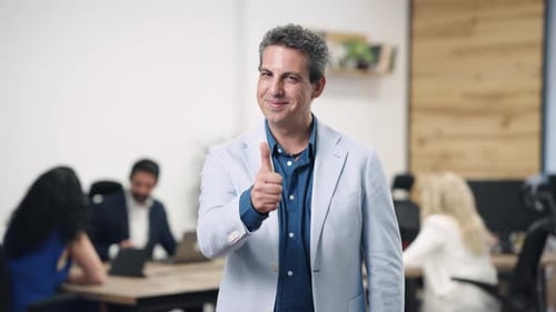 Successful Businessman Gesturing Thumbs Up While Winking in a Modern Office