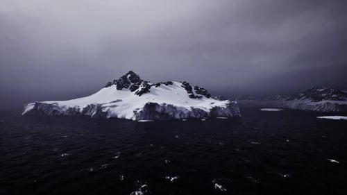 Flying Over Icy Ocean with Snowy Mountains and Dark Sky
