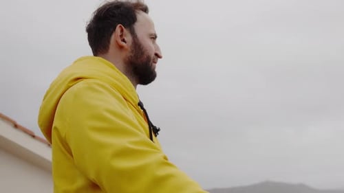 Man in Yellow Raincoat Looks at Overcast Sky