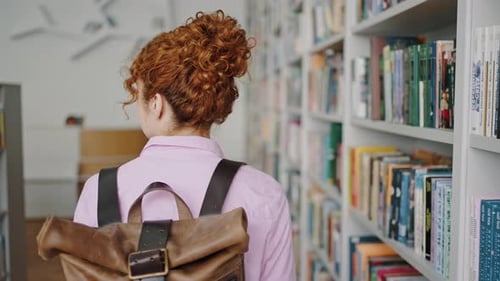 Female Student Walks Past Racks in Library Looking for Book
