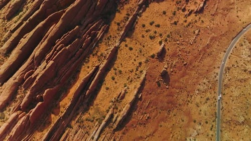 Cars driving by the road going along strangely shaped rocks. Orange desert with canyons in Utah, USA