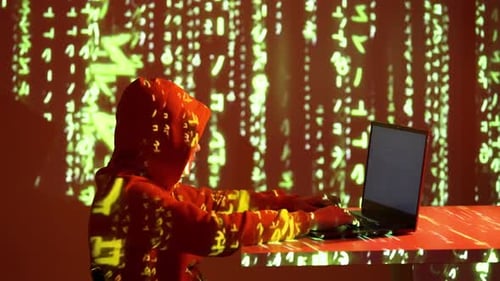 Hacker mascarado com capuz vermelho usando laptop em sala escura com código projetado e brilho cibernético