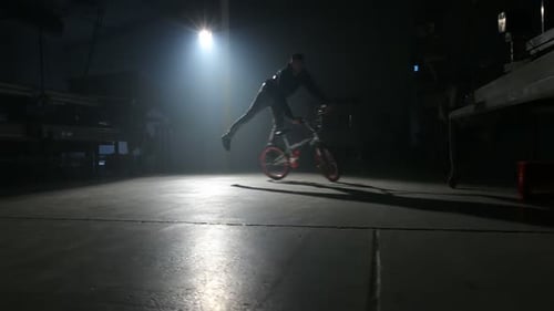 Young bmx rider performs extreme stunts in dark urban warehouse setting