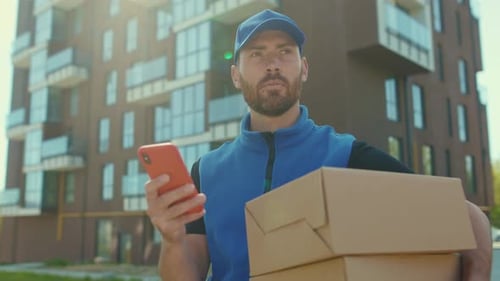 Handsome Young Man Delivery Texting Message on Smartphone Outdoor and Looking for Address Hold Box