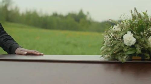 Hand on Coffin with Flowers in Rural Setting