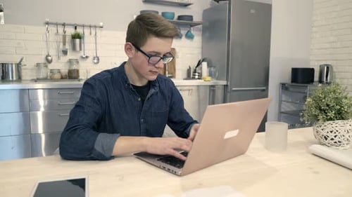 Teen Boy Typing on Laptop in Modern Kitchen
