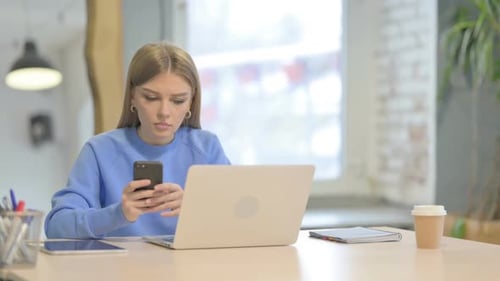 Young Adult Using Phone and Laptop in Office