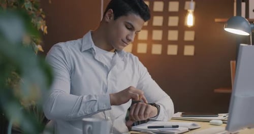 Middle Eastern Guy Using Smart Watch Touching Screen Using Modern Gadget in Office in Evening