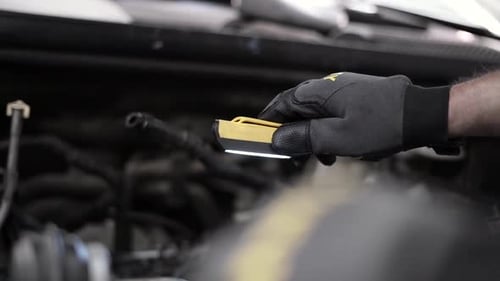 Low-angle shot of a mechanic using a light to check in a car engine bay