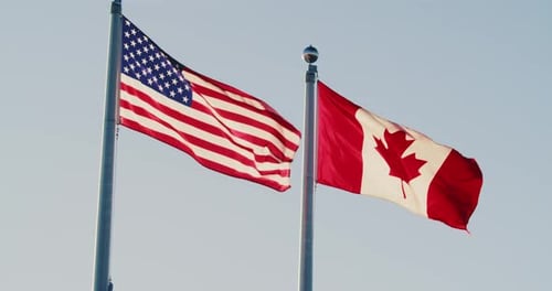American and Canadian Flags Waving Against Blue Sky