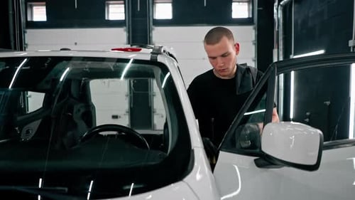 Close-up of a car wash worker using a plastic washing brush while cleaning the door card of a car
