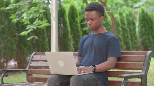 Casual African Man Doing Video Call on Laptop in Park