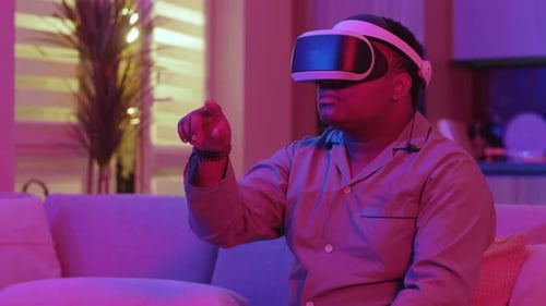 Close Up Serious Mixed Race Young Man Wearing Virtual Reality Headset Sitting on Sofa Choose Move