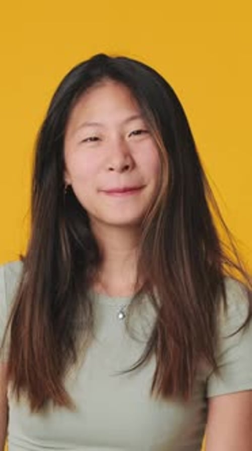 Young woman looking at camera, smiling and flirting isolated on yellow background in studio