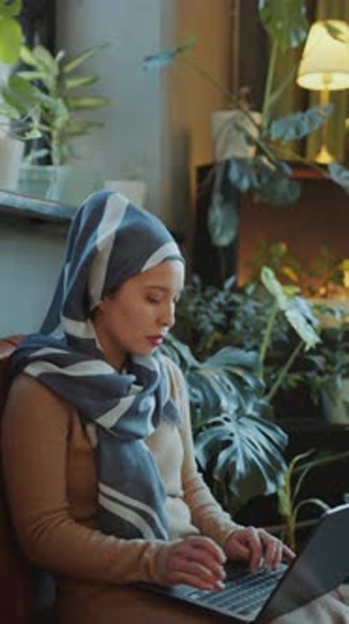 Muslim Woman in Hijab Typing on Laptop on Couch in Office