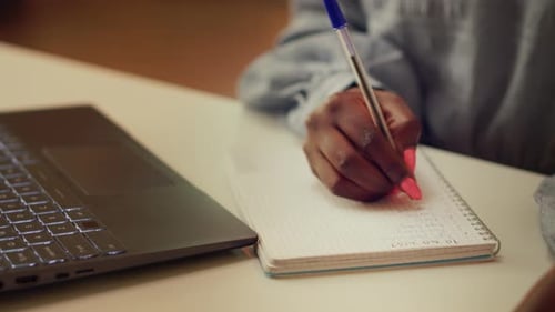 Woman Writes in Notebook Next to Laptop