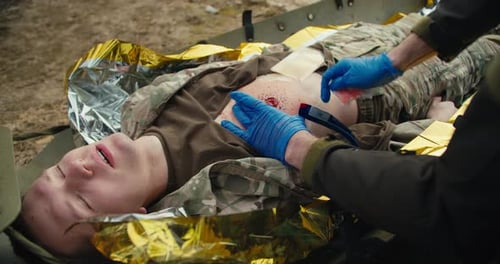 Un médico masculino seguro de sí mismo con guantes médicos azules detiene la sangre de un soldado herido con un camuflaje