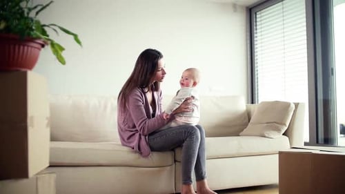 Eine junge Mutter mit einem Baby und Pappkartons zieht in ein neues Zuhause ein.