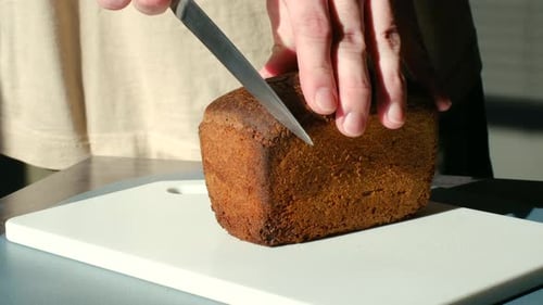 Person Cutting Brown Bread Loaf on Cutting Board
