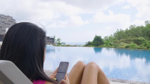 Female Guest With Smartphone Relaxing On Sun Lounger By The Poolside In Hotel. Uluwatu, Bali, Indone