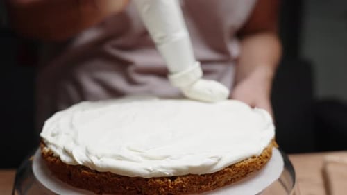 In slow motion, in a close-up shot, the woman is using a pastry bag to apply white cream