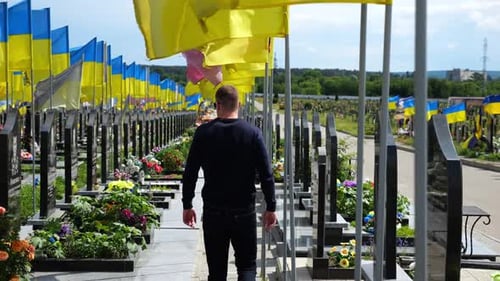 Mourning Man Go Among Countless Graves of Ukrainian Soldiers with National Flags at Military
