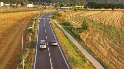 Long aerial drone shot of silver car on the asphalt road. A car drives through the countryside at su