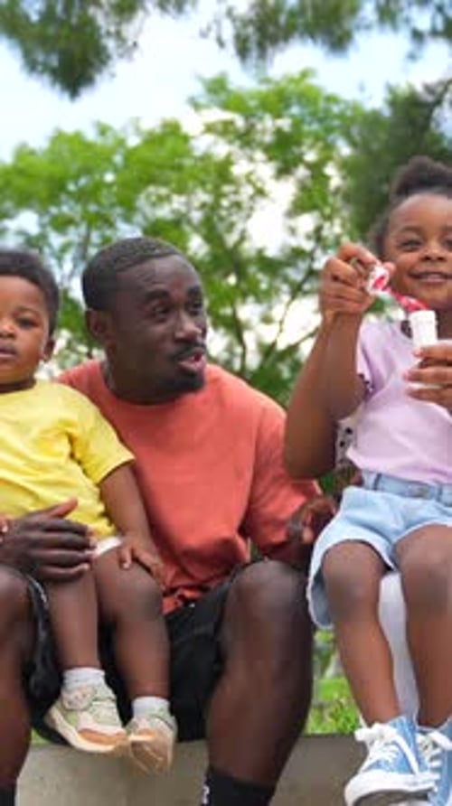 African black ethnic family with children in playground having fun blowing soap bubbles
