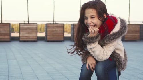Joyful Girl Bursts Into Laughter While Sitting on a City Street