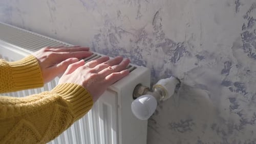 Closeup of Man Warming His Hands in Yellow Sweater on the Heater at Home During Cold Winter Days