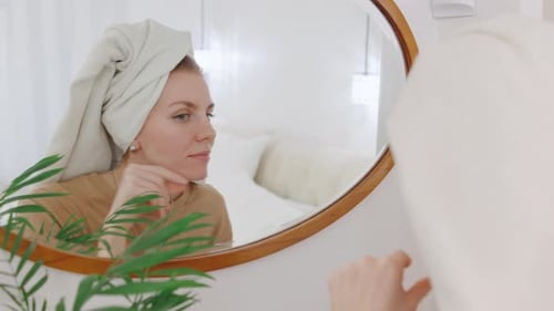 Woman Applies Facial Cream in Bright Bathroom