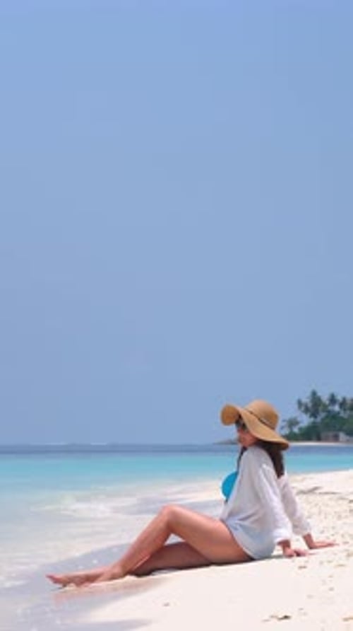 Woman Relax on Summer Resort Looking at the Ocean Wearing Straw Hat and White Shirt Sits on White