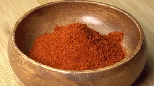 Paprika powder spice lies in wooden bowl and rotating on wooden board. Dry seasoning in spoon