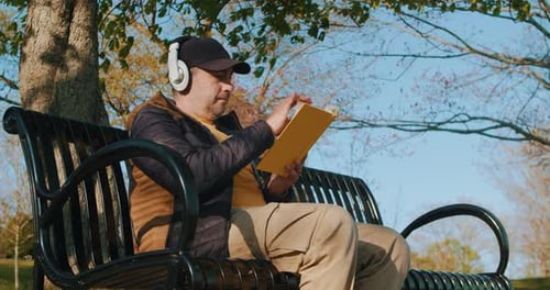 Mann liest ein Buch in der Natur und sitzt auf einer Parkbank