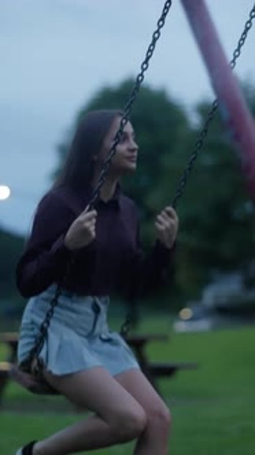 A Young Individual Revels in the Joy of Swinging Back and Forth in a Peaceful Park As Dusk