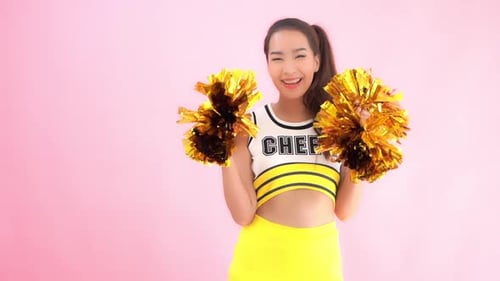A cute cheerleader in a uniform smiles while she shakes her sparkly pom-poms.
