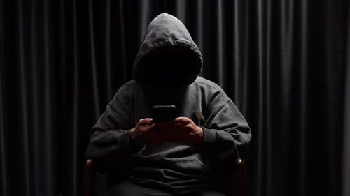 Hooded Figure Using Phone in Dark Interior