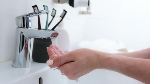 Adult Wipes and Washes Hands in White Sink